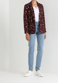 Bordowa marynarka w kwiaty zestawiona z białą bluzką, jasnoniebieskimi obcisłymi jeansami i białymi butami. Marynarka posiada kołnierz z wcięciem i otwarty przód.