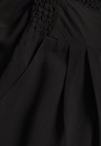 Tejido de vestido negro con detalle fruncido en la parte superior, con una textura suave y pliegues fluidos que se extienden desde la cintura.