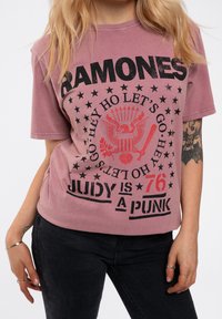 Pink cotton t-shirt with short sleeves, featuring a black graphic print of text and symbols including stars and an eagle design.