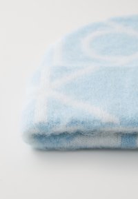 Lyseblåstrikket lue laget av mykt, fluffy garn med hvite geometriske mønstre. Stoffet ser koselig og varmt ut, ideelt for vinterbruk.