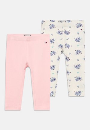 Two pairs of toddler leggings, one solid light pink, one white with purple and blue floral print, both with small Tommy Hilfiger logo.