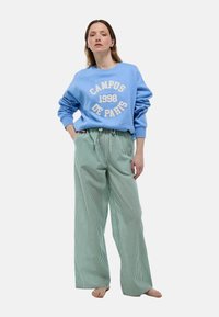 Sweat-shirt bleu clair avec le texte "CAMPUS 1998 DE PARIS" ; associé à un pantalon ample à rayures vertes ; coupe décontractée et texture douce.