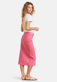 Pink denim skirt with a mid-length cut, featuring a high waist and a back pocket. Paired with a white graphic t-shirt and beige sandals.