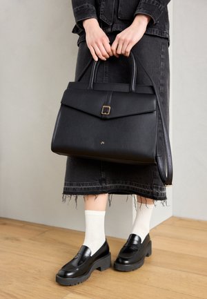 Sac à main structuré noir avec un rabat plié et des garnitures dorées. Texture en cuir lisse, poignées courtes sur le dessus et une bandoulière réglable.