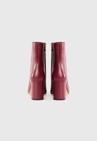 Stivaletti alla caviglia in pelle bordeaux con finitura lucida, tacco quadrato blocco e cerniere dorate sul retro, caratterizzati da un design snello.