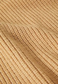 Hmotný pletený materiál v teplej, svetlohnedej farbe s vertikálnymi ryhami, ktorý vyžaruje mäkký a útulný vzhľad.