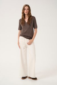 Hnedý krátky rukáv sveter s v-neck výstrihom, kombinovaný s bielymi širokými nohavicami a tmavohnedými platformovými topánkami, so voľným strihom a jemnou textúrou.