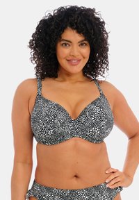 Zwart-witte bikini top met stippen, voorzien van schuimcups, verstelbare bandjes en een v-halsontwerp, gemaakt van een soepele stof.