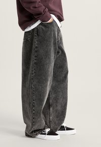 Zwarte baggy spijkerbroek met vervaagd was, vijf zakken ontwerp, zichtbare stiksels, gedragen door een persoon die zwarte sneakers draagt.