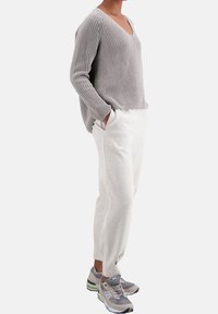 Pull gris en tricot avec col en V, coupe ample, associé à un pantalon de jogging gris clair, avec poches latérales et poignets élastiques. Porté avec des baskets grises.