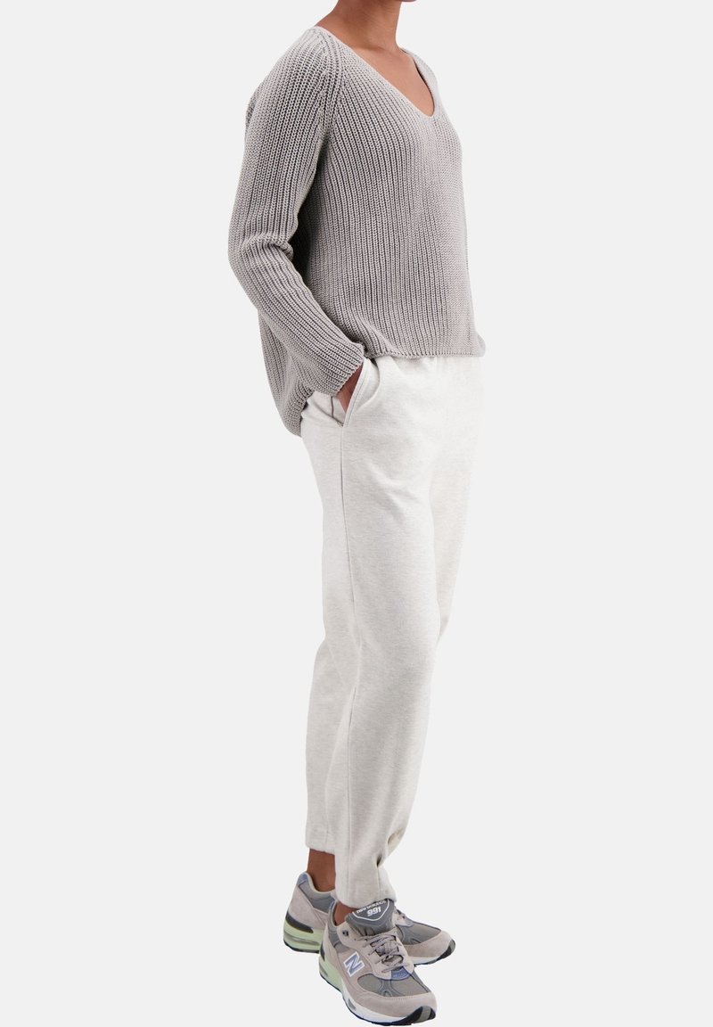 Pull gris en tricot avec col en V, coupe ample, associé à un pantalon de jogging gris clair, avec poches latérales et poignets élastiques. Porté avec des baskets grises.