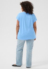 Light blue short-sleeve top with a relaxed fit, paired with light blue straight-leg jeans and black flats. Smooth fabric, minimal detailing.