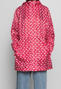 Czerwona wodoodporna kurtka z białym wzorem psów, z kapturem, długimi rękawami i kieszeniami bocznymi. Gładka, błyszcząca faktura.