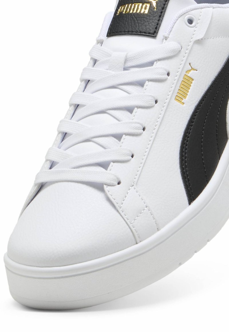 Weißer Sneaker mit strukturiertem Synthetik-Obermaterial, schwarzen Akzenten, Schnürdetails und einer weißen Gummisohle. Goldenes Logo auf der Zunge und an der Seite.