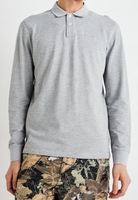 Man wearing long-sleeve light grey polo shirt paired with tan and green camouflage cargo pants.