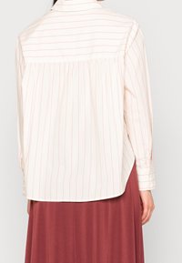 Blouse à manches longues à fines rayures crème et rose pâle, dotée d'un poignet boutonné, d’un ourlet arrondi et d’un détail froncé au dos.