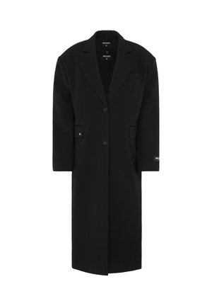 Manteau oversized noir avec un col à revers, fermeture à un bouton, poches avant et une texture lisse. Présente une étiquette de marque sur la manche.