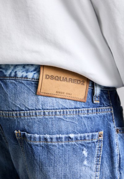 Blå denimjeans med en sliten struktur, prydda med en brun läderetikett präglad med "DSQUARED2" vid midjan.