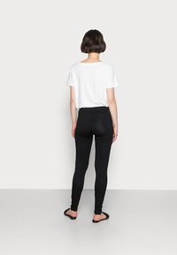 Leggings noirs à taille haute, texture lisse et coupe ajustée, associés à un t-shirt blanc uni et des sandales plates noires.