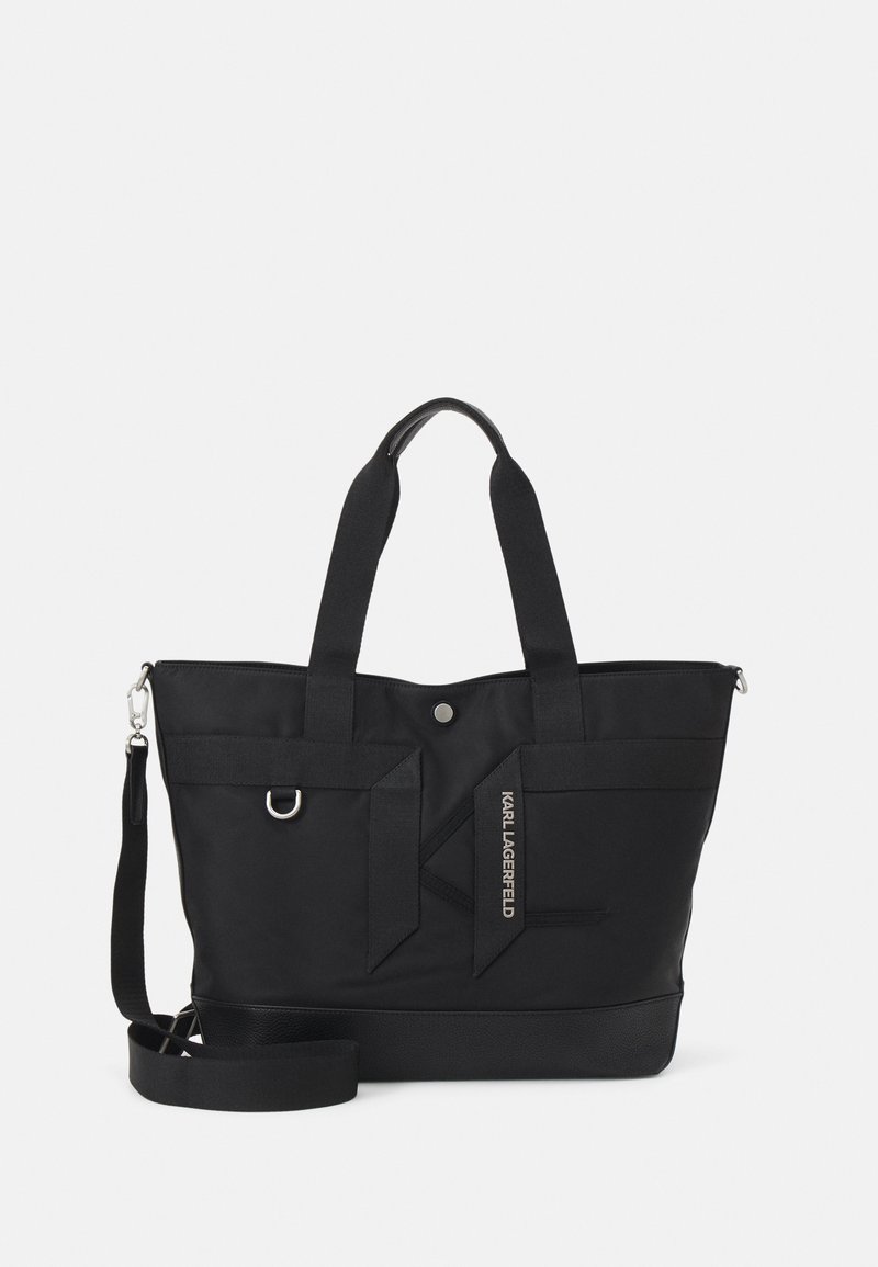 Czarna torba na ramię wykonana z wytrzymałego materiału, z dwiema uchwytami, odpinanym paskiem na ramię oraz detalem z logo. Gładka tekstura i solidna konstrukcja.