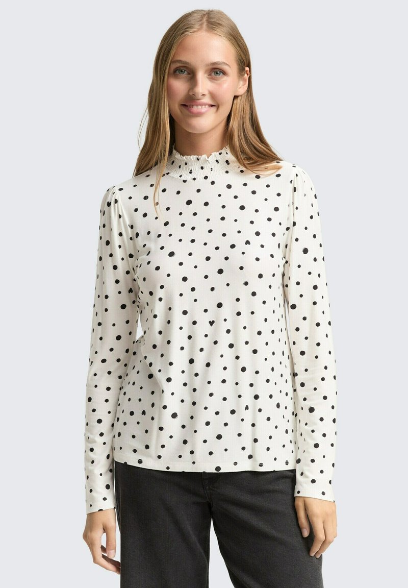 Weißes Langarmhemd mit schwarzen Punkten, ausgestattet mit einem gerafften, rüschenbesetzten Ausschnitt und einer glatten, weichen Stofftextur.