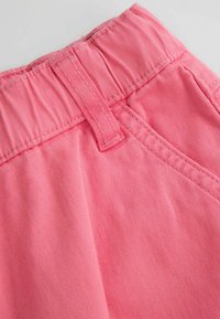 Zbliżenie różowej tkaniny z elastycznym paskiem w talii i przeszytym paskiem na odzieży.