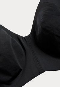 Sostenedor negro con tela suave, copas moldeadas y un diseño sin costuras. Presenta una costura central y un sutil detalle de costura a lo largo de los bordes.