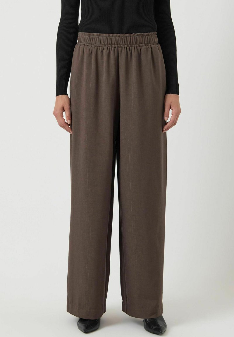 Bruine wijde broek met elastische tailleband, met een zachte textuur en subtiele verticale lijnen, gecombineerd met zwarte schoenen.
