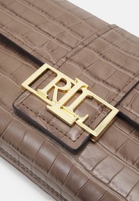 Brązowa torebka kopertówka z imitacji skóry krokodyla z złotym prostokątnym zapięciem z logo oraz gładką fakturą z przeszyciami.