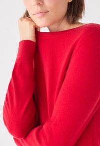 Maglione rosso in cashmere con scollatura a girocollo, texture morbida e maniche lunghe. La vista ravvicinata mette in evidenza la forma della manica e i dettagli della maglia fine.