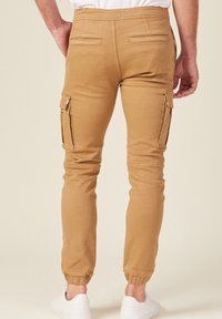 Khaki cargo byxor med tapered ben, elastiska ärmslut, dubbla sidofickor och dekorativ sömnad. Tillverkade av mjuk, hållbar bomullsblandning.