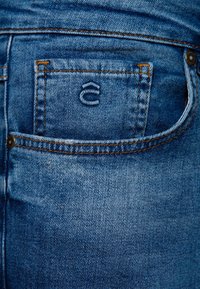 Modré džíny z denimu s zadní kapsou s logem, kontrastním oranžovým prošíváním a mírně vybledlou texturou.