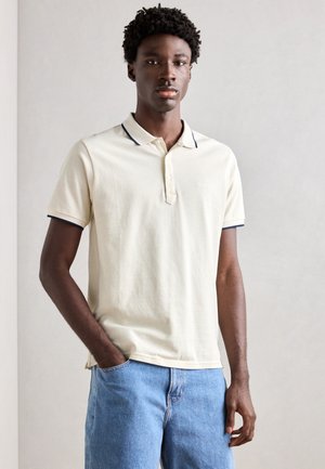 Polo shirt in light cream with navy accents at collar and sleeves, made from cotton, featuring a three-button placket and embroidered logo.