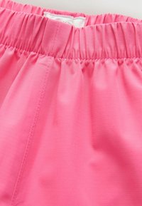 Nærbillede af en pink beklædningsliv med elastisk rynkning og synlige syninger på den glatte stofstruktur.