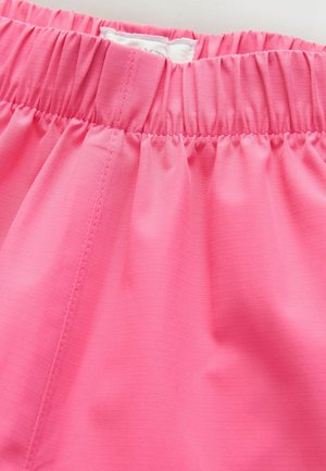 Krupni plan struka ružičastog odjevnog predmeta s elastičnim nabiranjem i vidljivim detaljima šivanja na glatkoj teksturi tkanine.