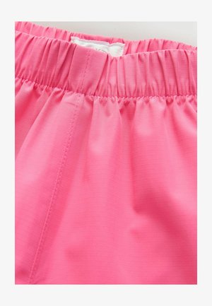 Közeli kép egy rózsaszín ruha derékrészéről, amely rugalmas ráncolással és látható varrási részletekkel rendelkezik a sima szövet textúráján.