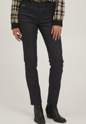 Námornícky modré slim-fit džínsy s hladkou textúrou, vybavené prednými vreckami a zipsom, skombinované s elegantnými čiernymi podpätkovými členkovými čižmami.
