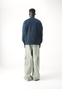 Felpa blu navy con polsini e orlo a coste, abbinata a pantaloni cargo in denim chiaro con tasche laterali e una vestibilità ampia.