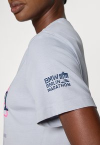 Hellgraues Baumwoll-T-Shirt mit dem Aufdruck "BMW BERLIN MARATHON" in Marineblau auf dem linken Ärmel. Kurze Ärmel und normale Passform.