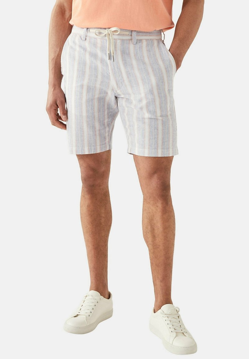 Pantaloni corti leggeri a righe nei colori blu, bianco e pesca. Presentano una cintura con lacci e tasche laterali. Abbinati a sneakers bianche.