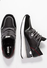 Czarno-szare sneakersy Michael Kors z białymi podeszwami, srebrnymi akcentami, czerwonymi detalami i wzorzystymi sznurowadłami przedstawione z widoków z góry i z boku.