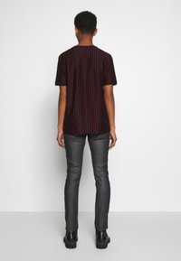 Herrskjorta med kort ärm i svart och röda vertikala ränder, matchad med grå slim-fit jeans och svarta ankelskor. Bakifrån visad.