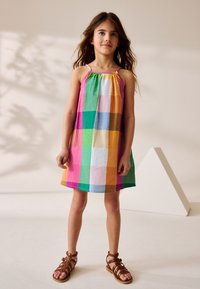 Robe à carreaux colorée avec une coupe décontractée, fabriquée en tissu léger. Caractérisée par des bretelles fines et un col froncé. Sandales marron à lanières.