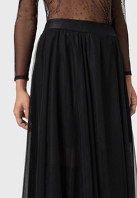 Jupe en tulle noir avec une taille ajustée, texture superposée et section supérieure transparente ornée. Présente des paillettes subtiles et un design fluide.