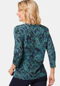Diepblauwe lange mouw top met een paisleypatroon in groen, turquoise en metallic accenten, met een relaxte pasvorm en ronde halslijn.
