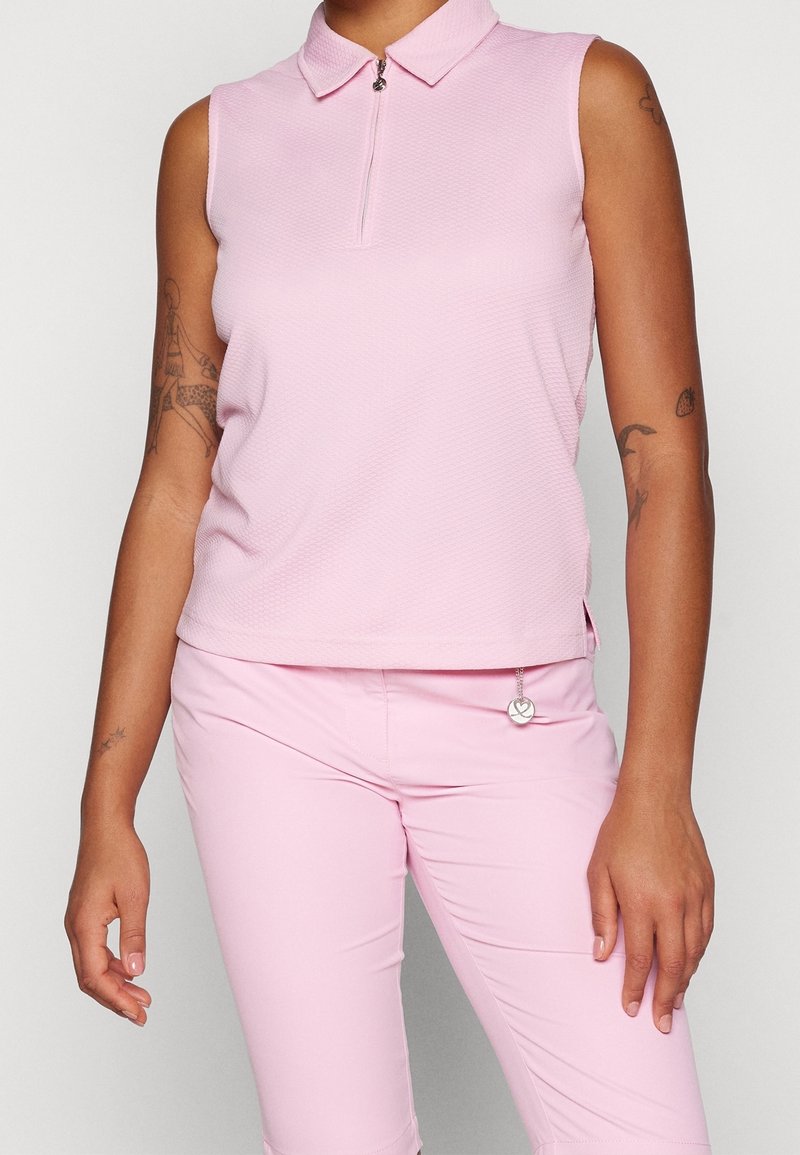 Ljust rosa ärmlös polo skjorta med krage, framdragkedjedetalj och texturerad tyg. Matchas med ljust rosa figurnära byxor.