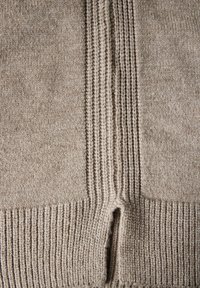 Béžový pletený svetr s žebrovanou texturou, který má vertikální pruhy a dvoucestné přední zapínání. Měkká, středně těžká příze.