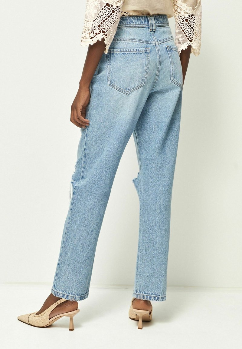 Vaaleansiniset korkeavyötäröiset farkut, joissa on löysä istuvuus, ja joissa on kulutettu yksityiskohtia sekä kaksi takataskua. Yhdistetty beigenvärisiin korkokenkiin.