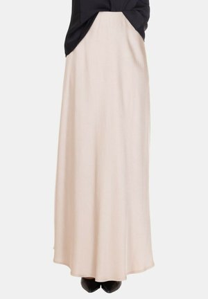 Gonna beige lunga abbinata a scarpe nere con punta e a un top nero annodato in vita.