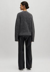 Grijze, fuzzy gebreide sweater met een ronde halslijn en een losse pasvorm, gecombineerd met zwarte, strakke, wijde broeken.